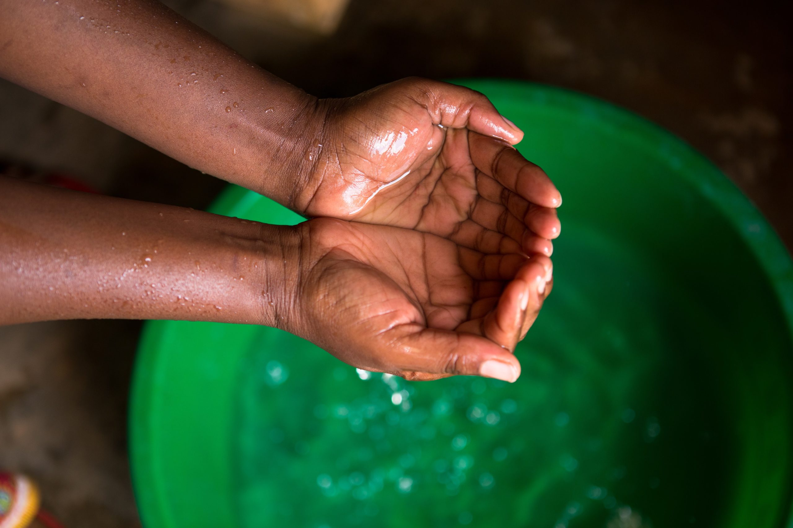Hands filled with water over a green bowl of clean water.